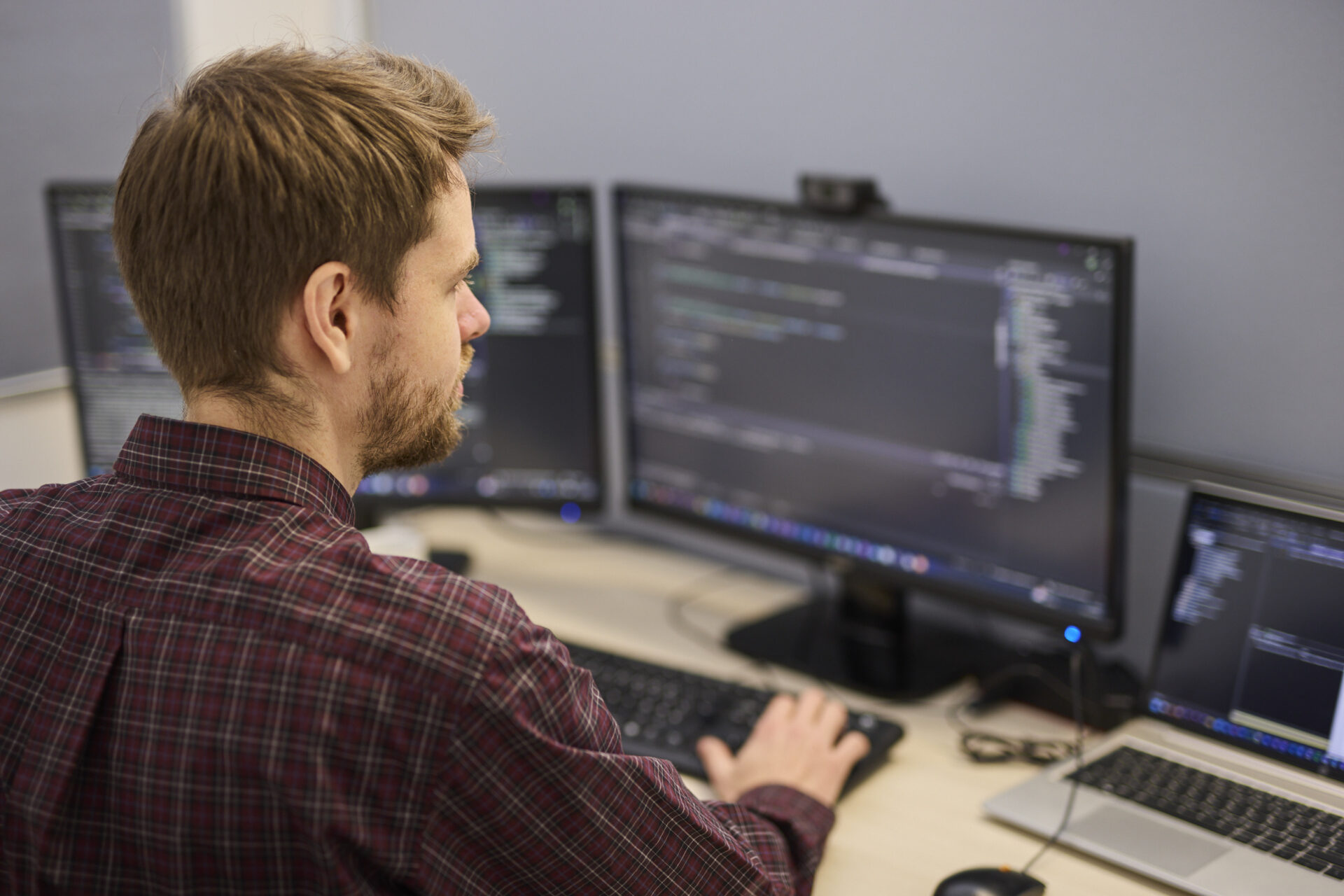 Person sitzt an einem Schreibtisch vor zwei Monitoren und programmiert an einer Software